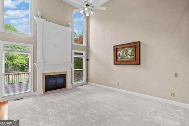 unfurnished living room with a towering ceiling, a fireplace with flush hearth, baseboards, a ceiling fan, and carpet