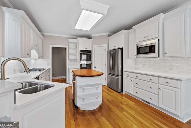 kitchen featuring open shelves, stainless steel appliances, a sink, light wood-style flooring, and ornamental molding
