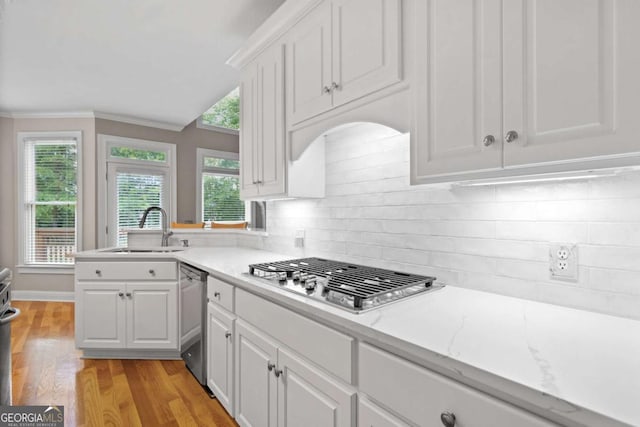 kitchen featuring a sink, stainless steel appliances, light wood-type flooring, white cabinets, and decorative backsplash