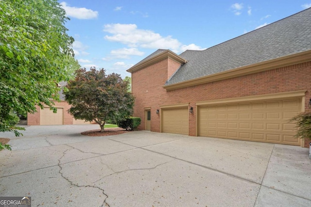 view of side of home featuring driveway, a shingled roof, brick siding, and a garage
