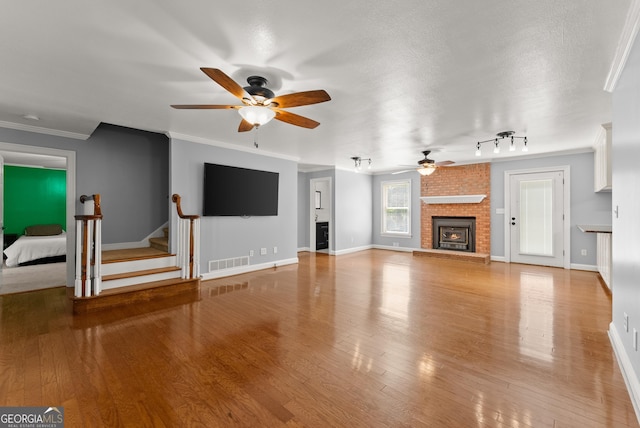 unfurnished living room featuring a ceiling fan, a fireplace, baseboards, ornamental molding, and wood finished floors