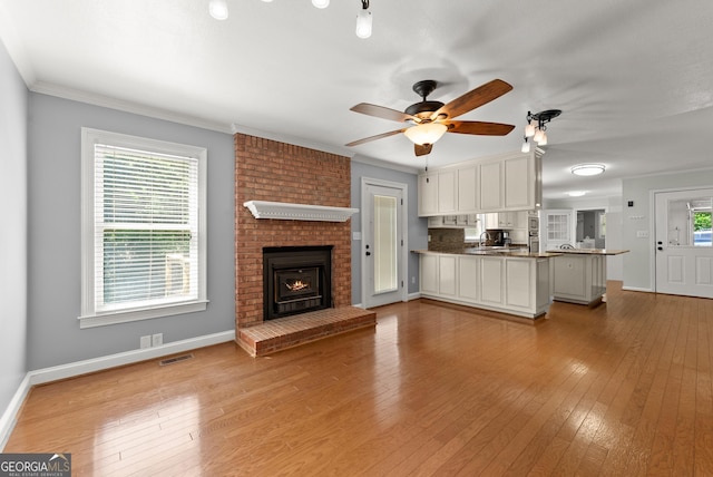 unfurnished living room with hardwood / wood-style floors, ceiling fan, baseboards, crown molding, and a fireplace