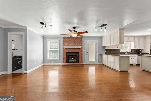 unfurnished living room featuring a sink, track lighting, a ceiling fan, ornamental molding, and plenty of natural light