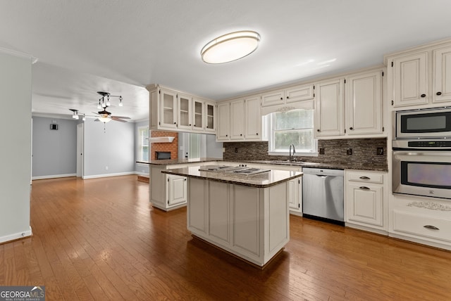 kitchen featuring appliances with stainless steel finishes, backsplash, a sink, a center island, and a ceiling fan