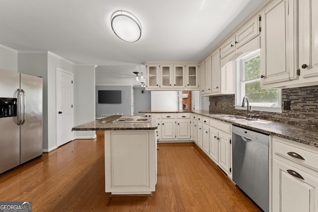 kitchen featuring appliances with stainless steel finishes, a sink, a peninsula, wood finished floors, and crown molding