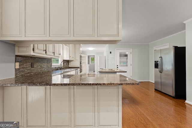 kitchen featuring stainless steel fridge with ice dispenser, a peninsula, a sink, ornamental molding, and dark stone counters
