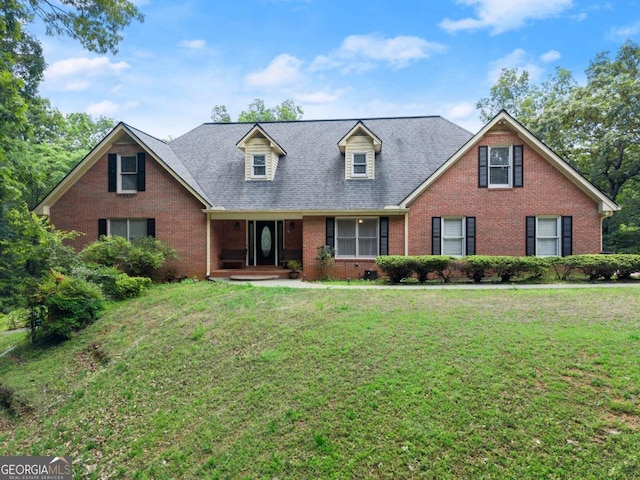 view of front facade with brick siding, a front yard, and a shingled roof