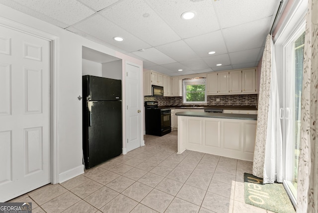 kitchen featuring black appliances, cream cabinets, a drop ceiling, dark countertops, and light tile patterned floors