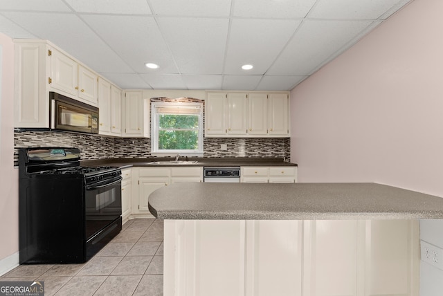 kitchen with black appliances, a paneled ceiling, dark countertops, a sink, and decorative backsplash