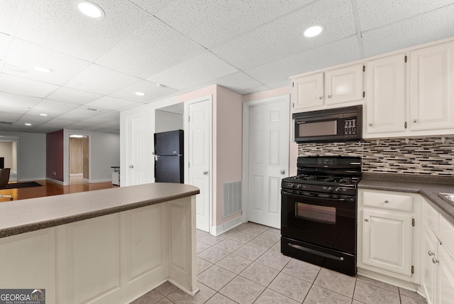 kitchen featuring black appliances, dark countertops, a paneled ceiling, light tile patterned flooring, and tasteful backsplash