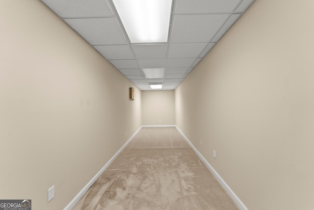 corridor with light colored carpet, a paneled ceiling, and baseboards