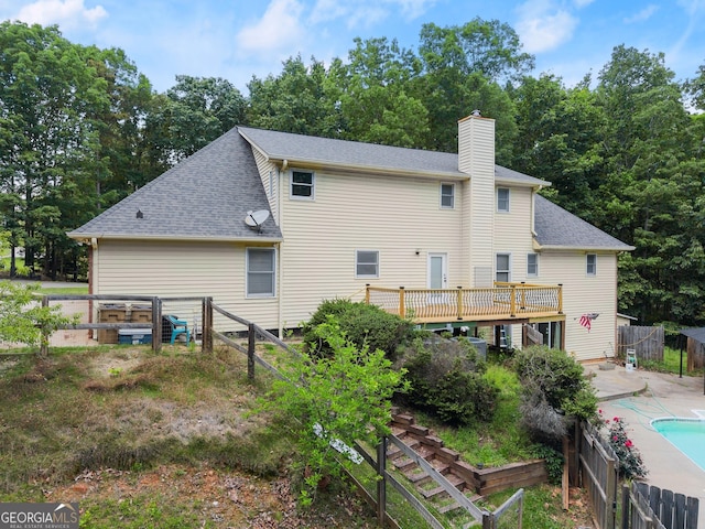 rear view of property with a chimney, roof with shingles, fence, and a wooden deck