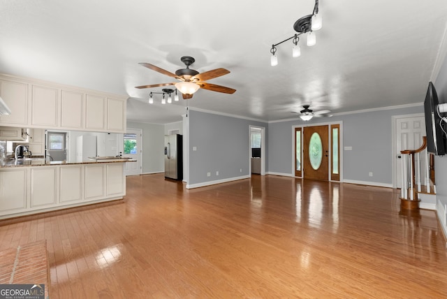 unfurnished living room featuring a ceiling fan, light wood finished floors, baseboards, stairs, and crown molding