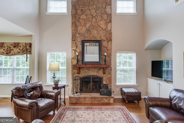 5960 Bridge Stone Ct, Cumming, GA 30028 - living room featuring a stone fireplace, a high ceiling, wood finished floors, arched walkways, and baseboards