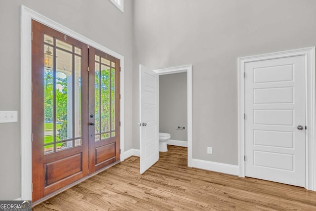 entrance foyer with french doors, light wood finished floors, baseboards, healthy amount of natural light, and a high ceiling