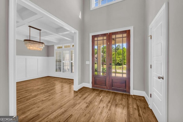 foyer featuring coffered ceiling, plenty of natural light, wood finished floors, beamed ceiling, and a chandelier