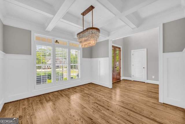unfurnished dining area featuring coffered ceiling, a decorative wall, wood finished floors, and a chandelier