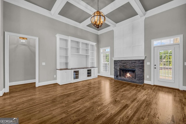 unfurnished living room with a chandelier, a high ceiling, plenty of natural light, coffered ceiling, and a stone fireplace