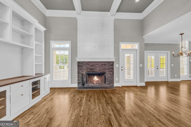 unfurnished living room featuring a fireplace, crown molding, a towering ceiling, a chandelier, and wood finished floors