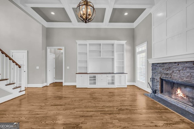 unfurnished living room with stairs, a chandelier, a stone fireplace, baseboards, and beamed ceiling