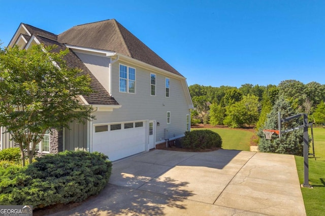 view of home's exterior featuring driveway, a garage, roof with shingles, and a lawn