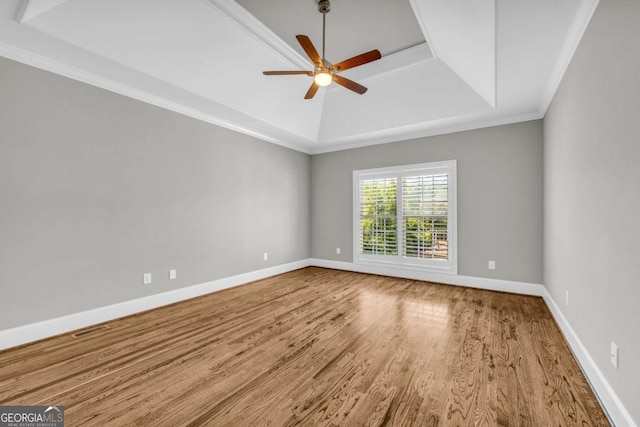 empty room featuring a tray ceiling, wood finished floors, a ceiling fan, baseboards, and ornamental molding
