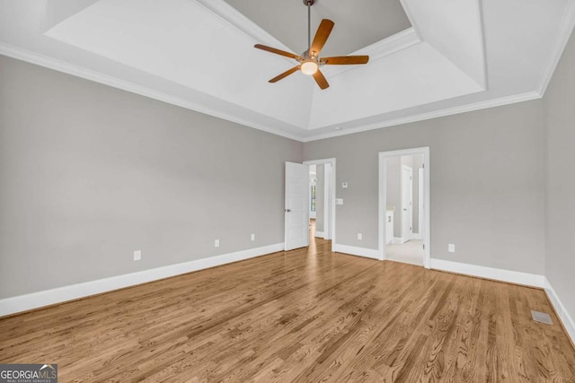 empty room featuring a tray ceiling, wood finished floors, a ceiling fan, baseboards, and ornamental molding