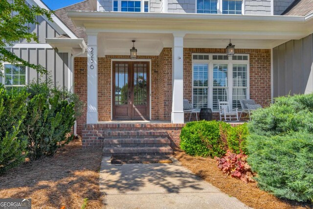 doorway to property with board and batten siding, brick siding, and covered porch