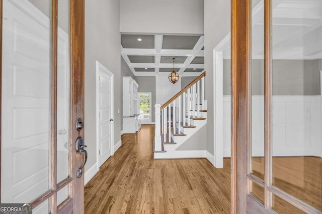 foyer entrance with coffered ceiling, light wood-type flooring, baseboards, beam ceiling, and stairs