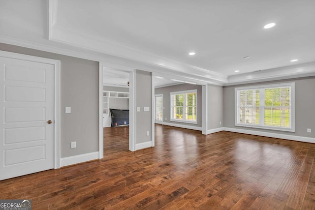 unfurnished living room featuring crown molding, wood finished floors, baseboards, recessed lighting, and a raised ceiling