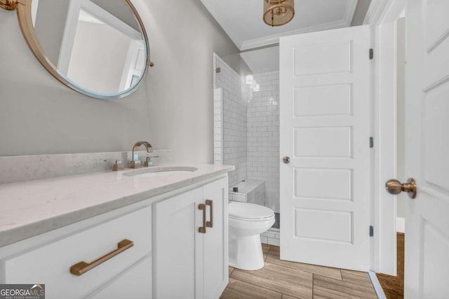 bathroom with a tile shower, toilet, vanity, crown molding, and wood finished floors