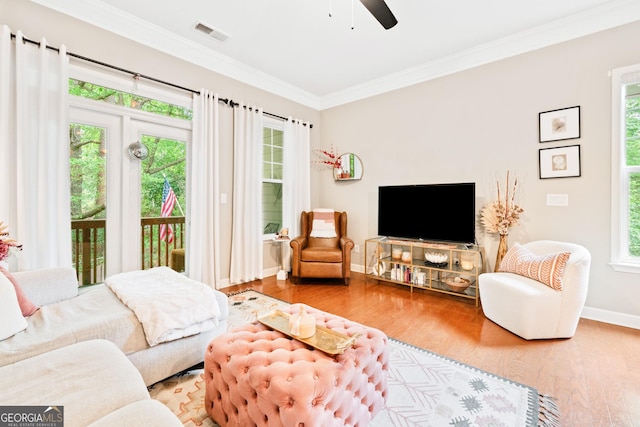 living area featuring ornamental molding, wood finished floors, ceiling fan, baseboards, and plenty of natural light