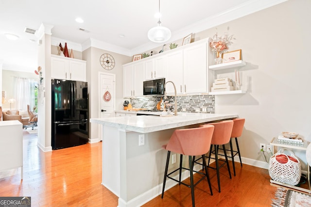 kitchen with black appliances, a peninsula, ornamental molding, a breakfast bar area, and white cabinetry