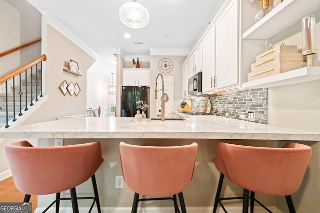 kitchen with a peninsula, decorative backsplash, white cabinetry, freestanding refrigerator, and ornamental molding