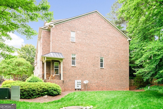 view of home's exterior featuring brick siding, a lawn, and a standing seam roof
