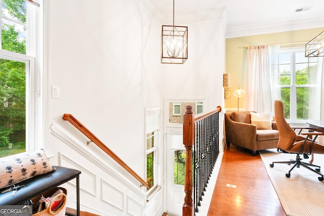 living area with an upstairs landing, a chandelier, ornamental molding, and light wood-style flooring