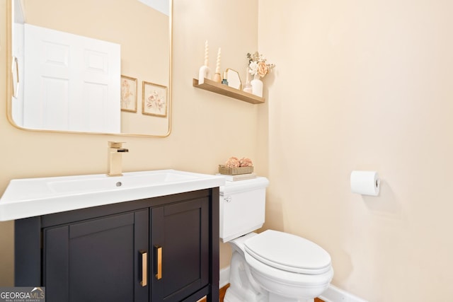 half bath with toilet, baseboards, and vanity