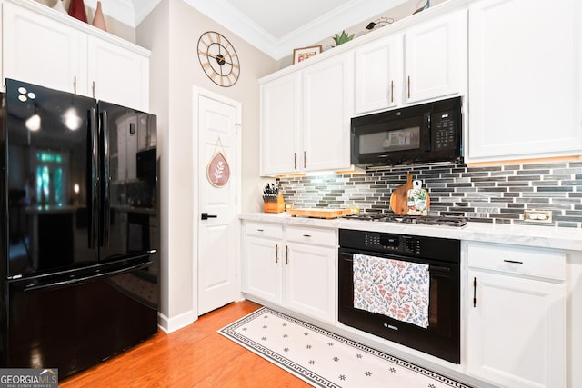 kitchen with black appliances, ornamental molding, light wood-style floors, white cabinets, and backsplash