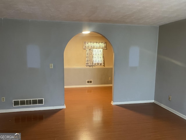 spare room with arched walkways, wood finished floors, baseboards, and a textured ceiling