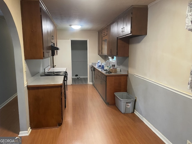 kitchen with light wood finished floors, electric stove, light countertops, arched walkways, and under cabinet range hood
