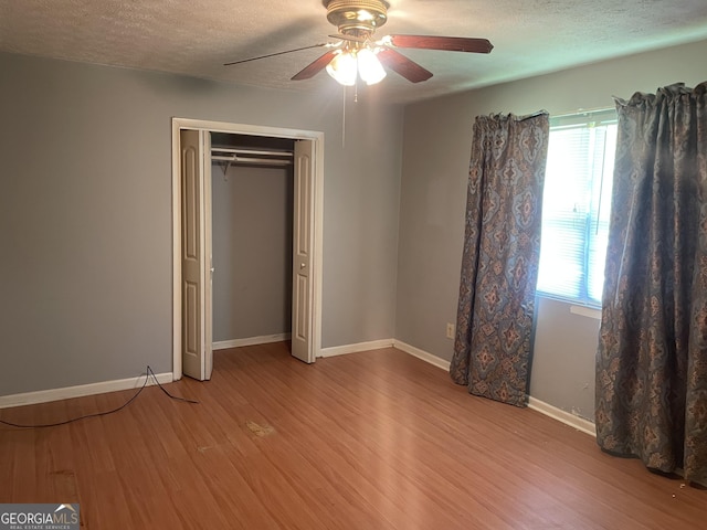 unfurnished bedroom featuring wood finished floors, a textured ceiling, ceiling fan, baseboards, and a closet
