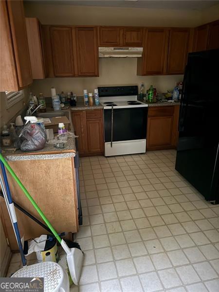 kitchen with range with electric cooktop, freestanding refrigerator, under cabinet range hood, brown cabinets, and light countertops