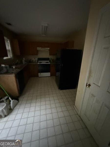 kitchen featuring electric range oven, fridge, under cabinet range hood, light flooring, and brown cabinets