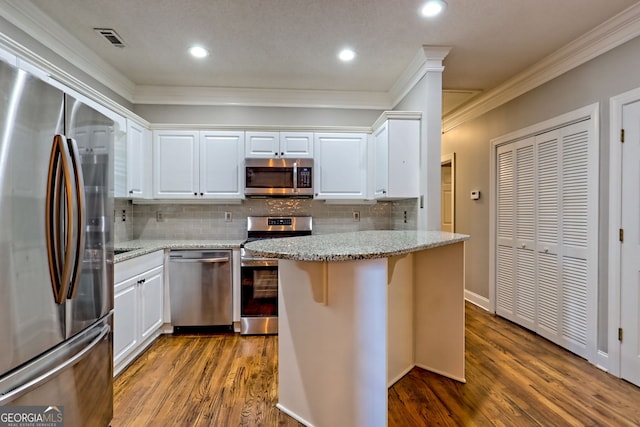 kitchen with appliances with stainless steel finishes, ornamental molding, dark wood finished floors, white cabinets, and decorative backsplash