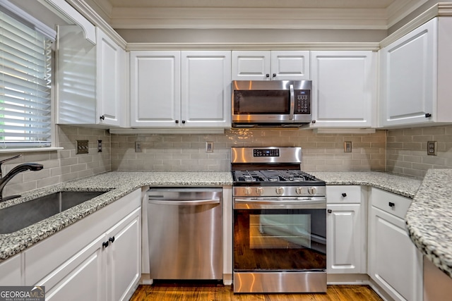 kitchen with appliances with stainless steel finishes, a sink, white cabinetry, backsplash, and light stone countertops