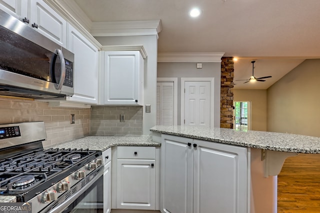 kitchen with stainless steel appliances, ceiling fan, a peninsula, backsplash, and white cabinets