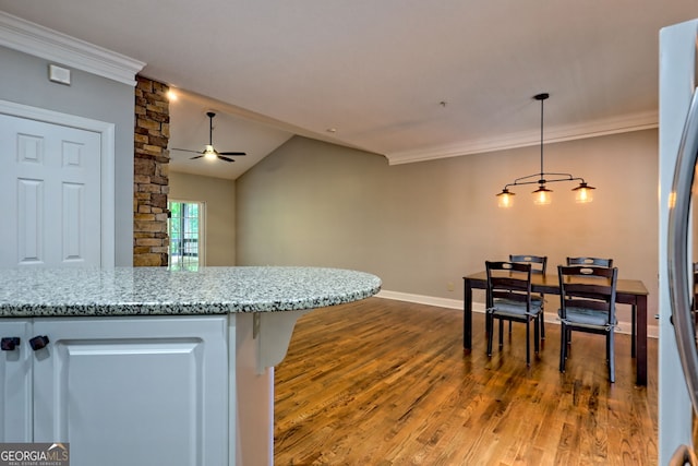 kitchen with wood finished floors, ceiling fan, light stone counters, crown molding, and baseboards