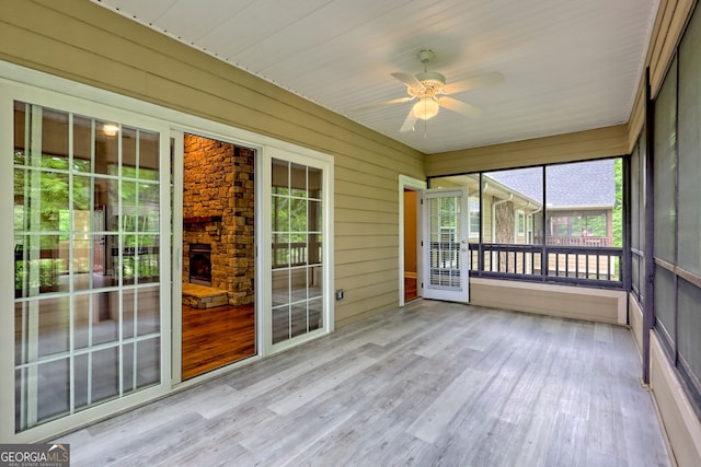 unfurnished sunroom featuring a ceiling fan and an outdoor stone fireplace