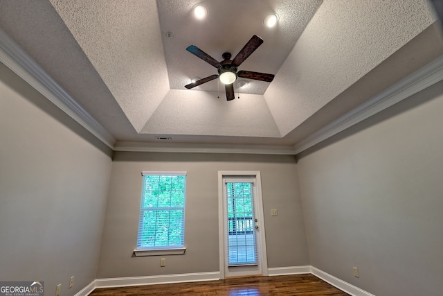 unfurnished room with dark wood-type flooring, ceiling fan, a tray ceiling, crown molding, and a textured ceiling