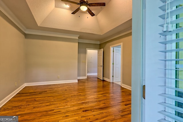 empty room featuring dark wood finished floors, a ceiling fan, crown molding, a raised ceiling, and baseboards